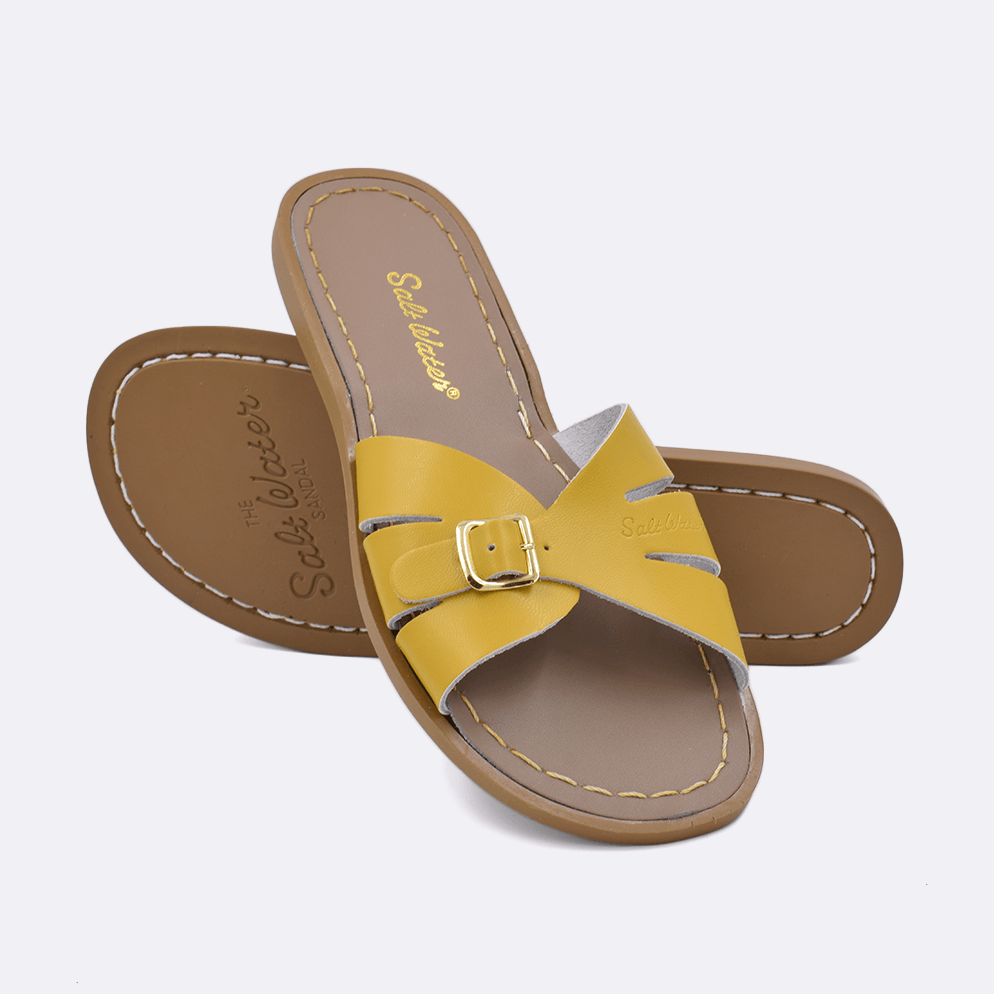 Two 9900 Classic Slide style sandals color mustard.  One standing with the sole facing the camera. The second is laying diagonally over the top left edge of the sole.	Adult Size.