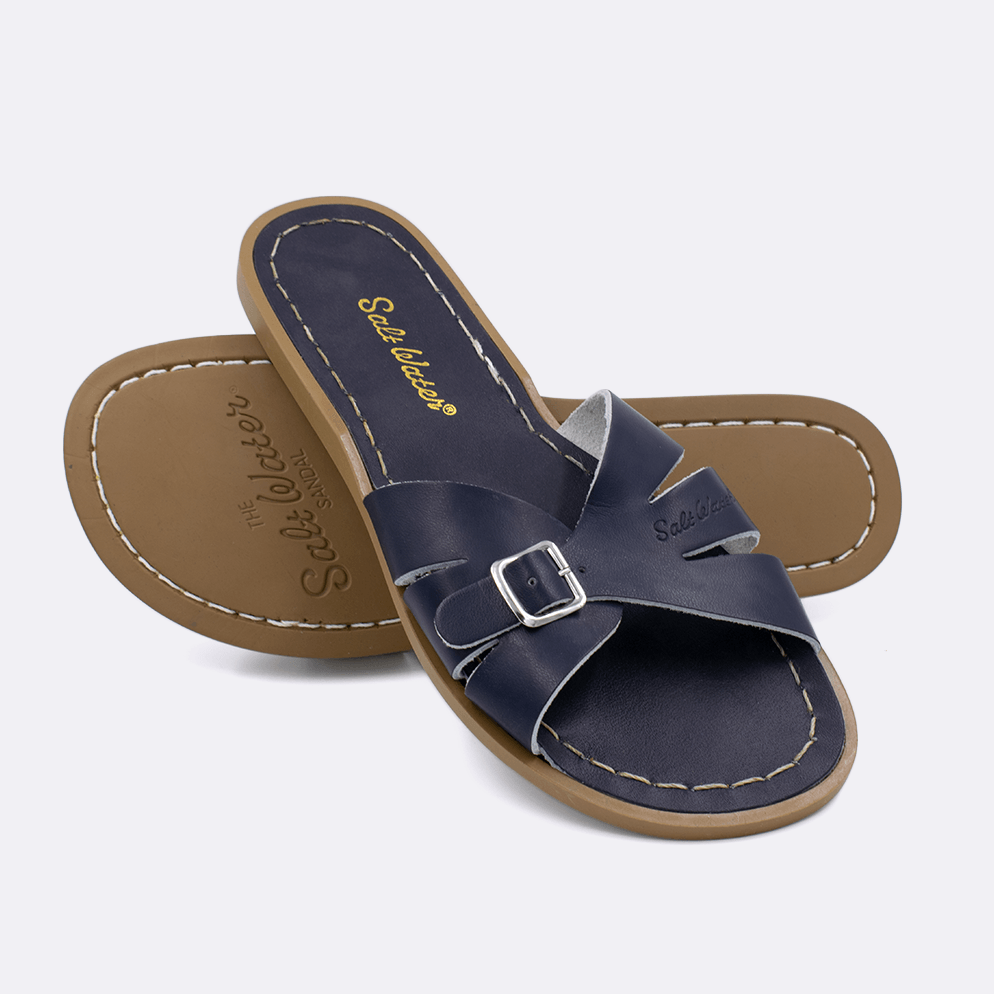 Two 9900 Classic Slide style sandals color navy.  One standing with the sole facing the camera. The second is laying diagonally over the top left edge of the sole.	Adult Size.
