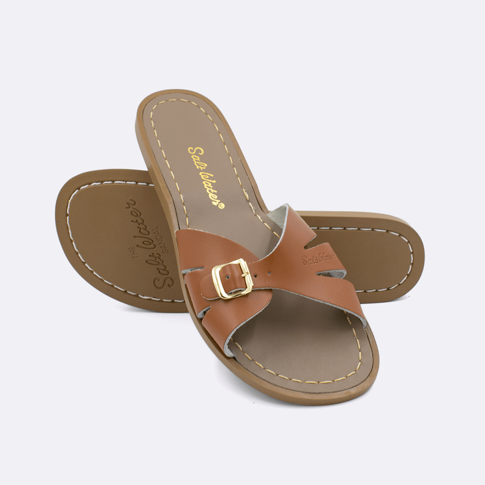 Two 9900 Classic Slide style sandals color tan.  One standing with the sole facing the camera. The second is laying diagonally over the top left edge of the sole.	Adult Size.